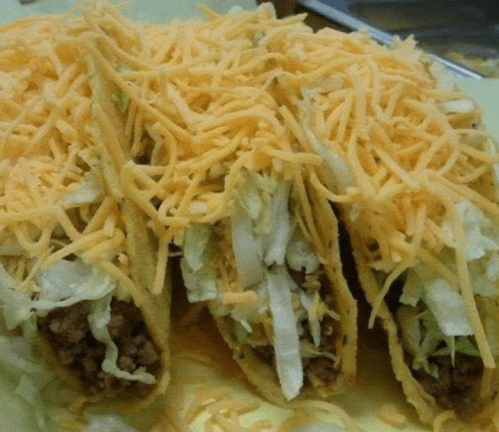 Three tacos filled with seasoned meat, topped with shredded lettuce and a generous layer of cheese.