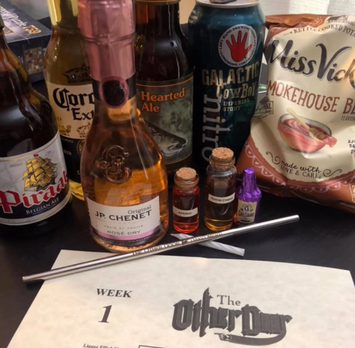 A collection of drinks, snacks, and a weekly planner on a table, featuring various bottles and a straw.