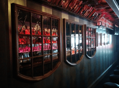 A dimly lit bar with decorative mirrors and a colorful backlit shelf of bottles.