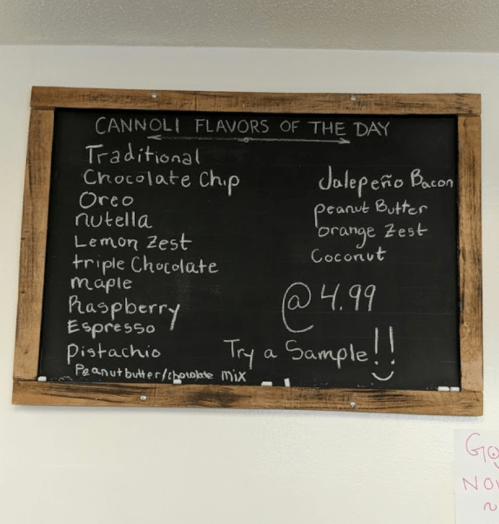 Chalkboard menu listing cannoli flavors of the day, including traditional, chocolate chip, and jalapeño bacon.