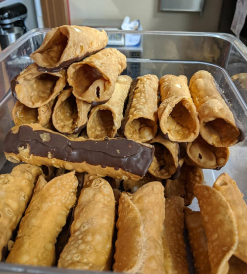 A clear container filled with various cannoli shells, some plain and others dipped in chocolate.