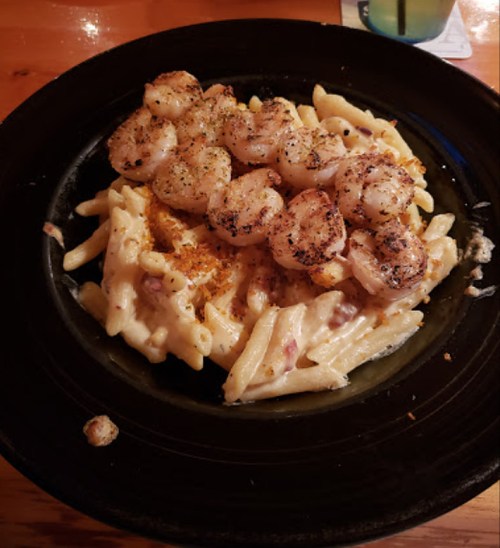 A plate of creamy pasta topped with grilled shrimp and crispy breadcrumbs, served on a black dish.