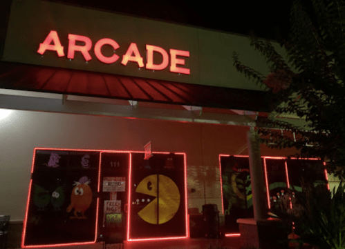 Brightly lit arcade entrance at night, featuring colorful murals and neon lights. Sign reads "ARCADE."