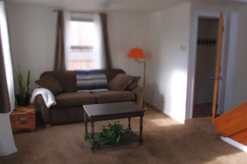 Cozy living room with a brown couch, coffee table, lamp, and a staircase leading to another room.