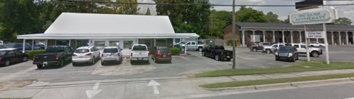 A restaurant with a white roof and parking lot filled with cars, located on a tree-lined street.