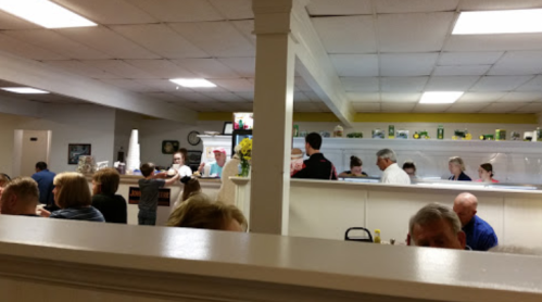 A busy restaurant interior with diners at tables and staff serving food in a casual setting.