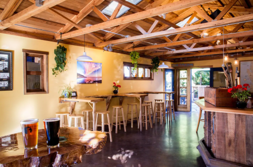 Cozy interior of a bar with wooden beams, stools, and two glasses of beer on a table. Bright and inviting atmosphere.
