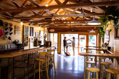 A cozy café interior with wooden beams, a bar area, and two people chatting near the entrance.