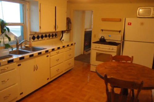 A cozy kitchen featuring white cabinets, a wooden table, and appliances including a stove and refrigerator.