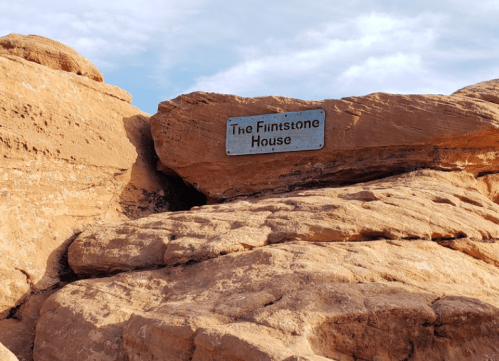Sign reading "The Flintstone House" mounted on a large rock formation under a blue sky.