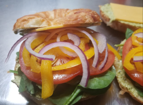 A close-up of a sandwich with layers of spinach, tomato, yellow and red bell peppers, and red onion on a croissant.