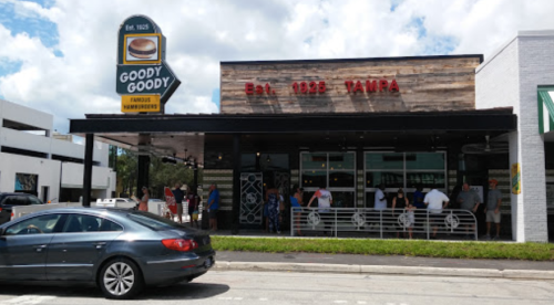 Exterior of Goody Goody restaurant in Tampa, with a line of customers outside and a car parked in front.