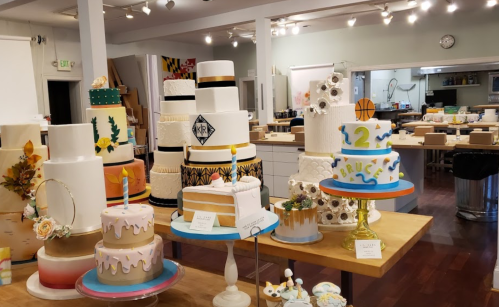 A variety of decorated cakes displayed on tables in a bright, spacious bakery studio.