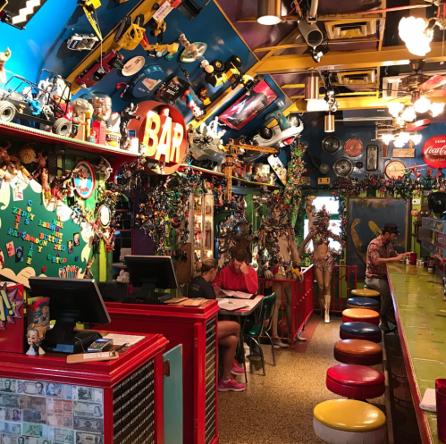 Colorful diner interior with eclectic decor, a bar area, and patrons enjoying their meals at a vibrant counter.