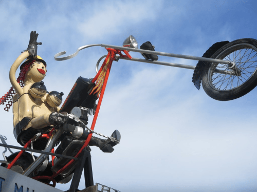 A whimsical motorcycle sculpture featuring a figure with a red wig, riding a chopper with one wheel raised.