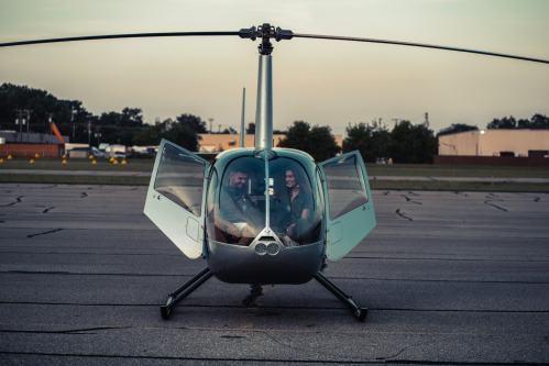 A helicopter on a runway with two people inside, doors open, during sunset.