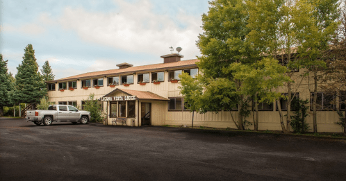 A two-story building with a sign reading "Lakeside Vista Lodge," surrounded by trees and parked vehicles.