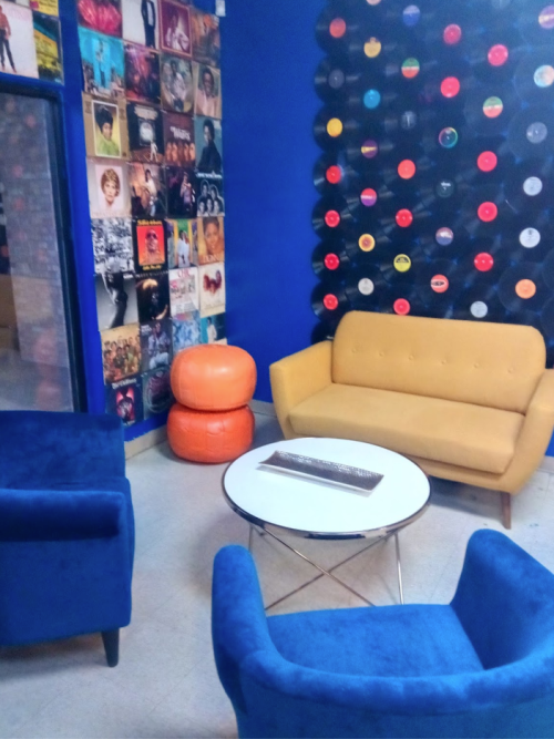 A cozy lounge area with a yellow sofa, blue chairs, and a wall of colorful vinyl records.