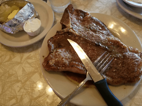 A large steak on a plate with a knife and fork, accompanied by a baked potato with butter on the side.
