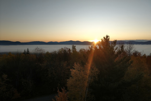 Sunrise over misty mountains, with vibrant autumn trees in the foreground and a warm glow in the sky.