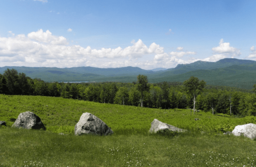 A scenic view of rolling green hills, large rocks in the foreground, and a blue sky with fluffy clouds.