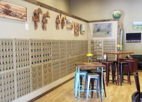 A cozy café interior featuring a wall of mailboxes, wooden decor, and small tables with flowers.