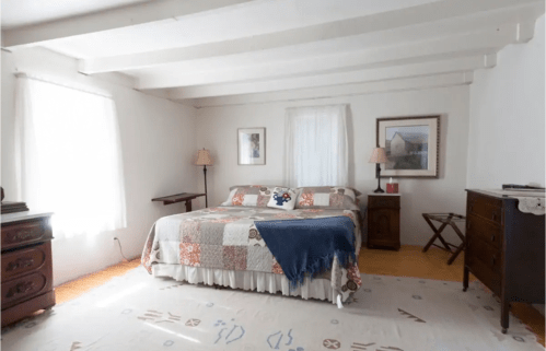 Bright, minimalist bedroom with a quilted bedspread, wooden furniture, and soft natural light.