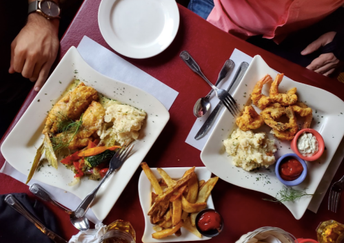 Two plates of seafood dishes with shrimp, fish, and sides of rice and fries, served on a red table.