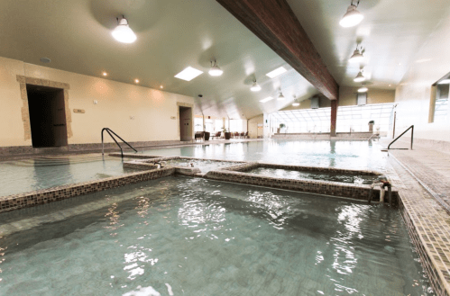 Indoor spa area with multiple pools, natural light, and a wooden beam ceiling. Relaxing atmosphere.
