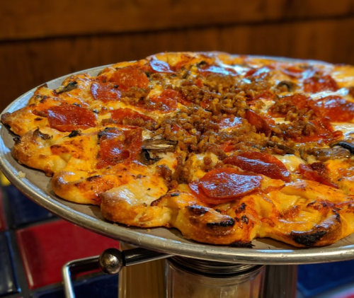 A freshly baked pizza topped with pepperoni and sausage on a silver serving tray.