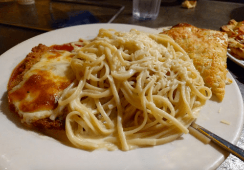 A plate of spaghetti with creamy sauce, chicken parmesan, and a slice of cheesy garlic bread.