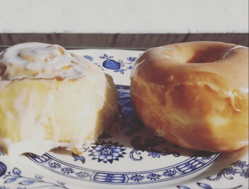 A cinnamon roll with icing next to a glazed donut on a decorative blue and white plate.