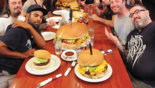 A group of people at a table with oversized burgers, smiling and posing for the camera.