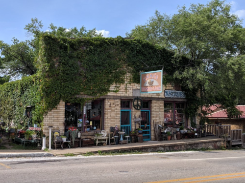 A charming, ivy-covered storefront with a sign, surrounded by greenery and outdoor seating.