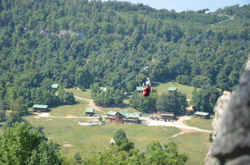 A person zip-lining over a lush green landscape with cabins and trees in the background.