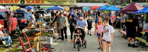 A bustling flea market scene with people walking, vendors under colorful tents, and various items for sale.