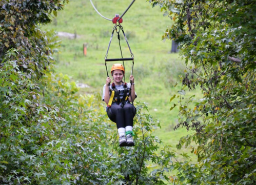 A person in a helmet and harness zip-lining through a lush green landscape.