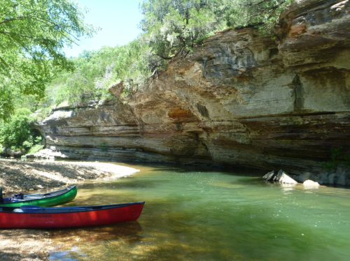 A serene river scene with two canoes on the shore, surrounded by lush greenery and rocky cliffs.