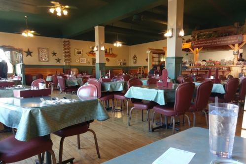 A spacious, empty restaurant with green checkered tables, red chairs, and rustic decor, featuring wooden beams and star accents.