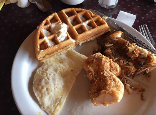 A plate with a waffle topped with butter, fried eggs, crispy chicken, and hash browns.