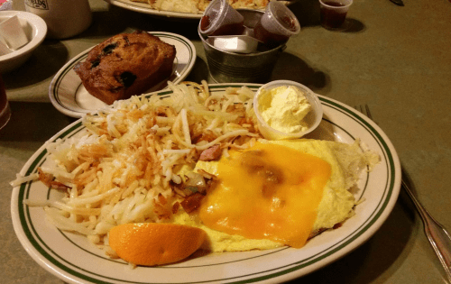 A plate of breakfast featuring an omelet with cheese, hash browns, an orange slice, and a muffin on the side.