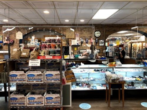 A cozy shop interior with shelves of chocolates and candies, featuring a display case and a cashier in the background.