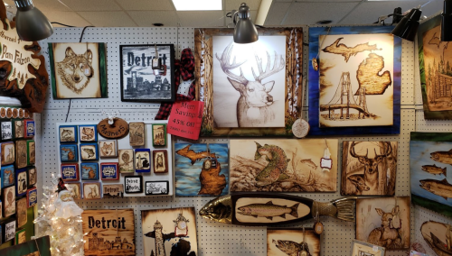 A display of wooden art featuring wildlife, landscapes, and Detroit-themed pieces, with a sale sign for 45% off.