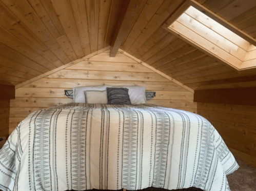 Cozy attic bedroom with a wooden ceiling, skylights, and a patterned bedspread on a large bed.