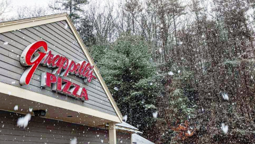 A snowy scene featuring the sign of Grappelli's Pizza against a backdrop of trees.