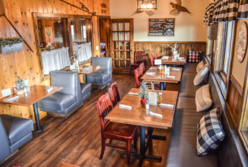 Cozy restaurant interior with wooden walls, tables, and booths, featuring rustic decor and a warm atmosphere.
