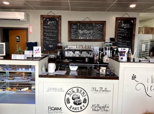 A cozy bakery counter with a coffee machine, menu boards, and display cases filled with pastries and sweets.