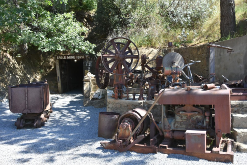 Historic mining equipment displayed outside the entrance of Eagle Mine, established in 1870, surrounded by greenery.