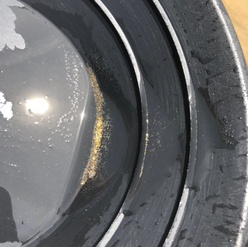 Close-up of a black pan with water, showing a small amount of gold dust settled at the bottom.