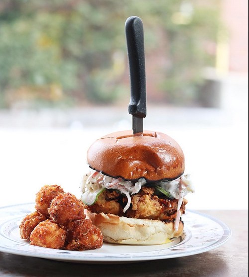 A crispy chicken sandwich with coleslaw on a bun, served with golden tater tots on the side.